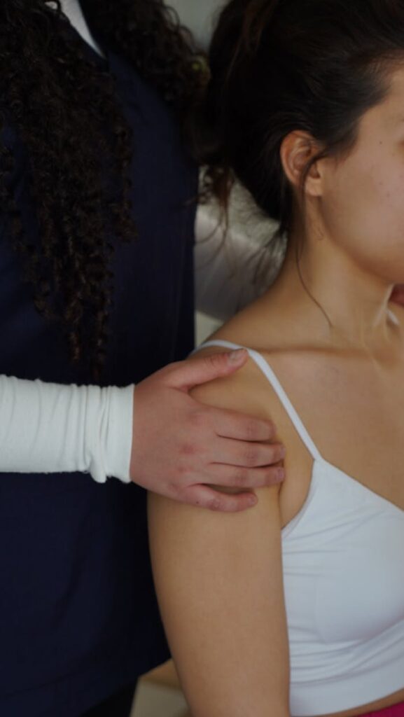 A physiotherapist adjusts a woman's shoulder during a therapy session indoors.